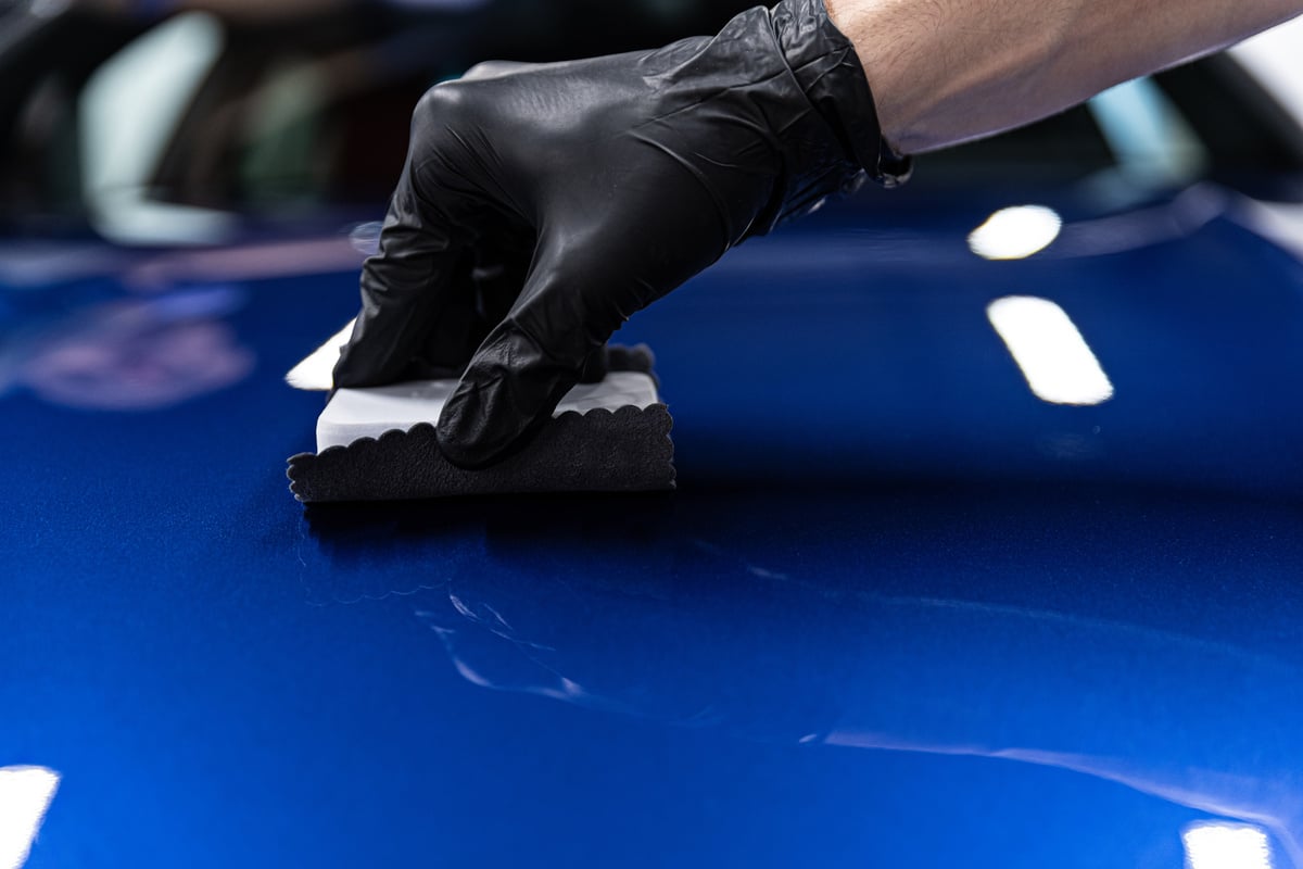 Man worker of car detailing studio applying ceramic coating on car paint with sponge applicator.